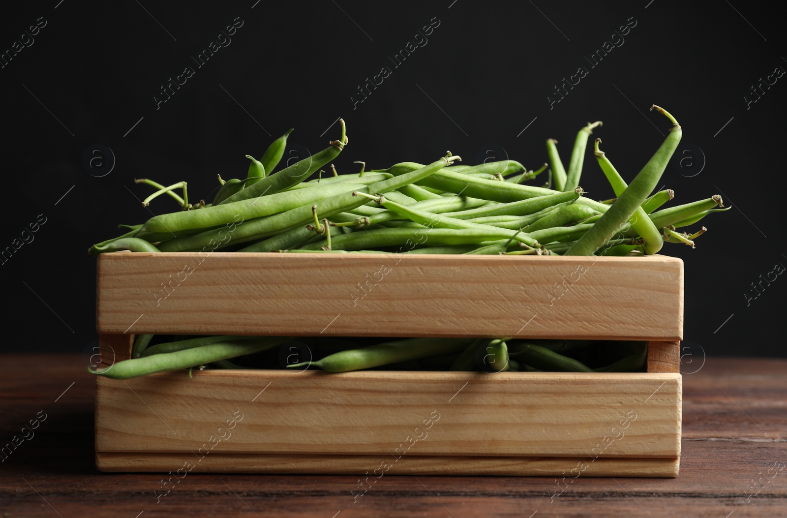 Photo of Fresh green beans in crate on wooden table against black background