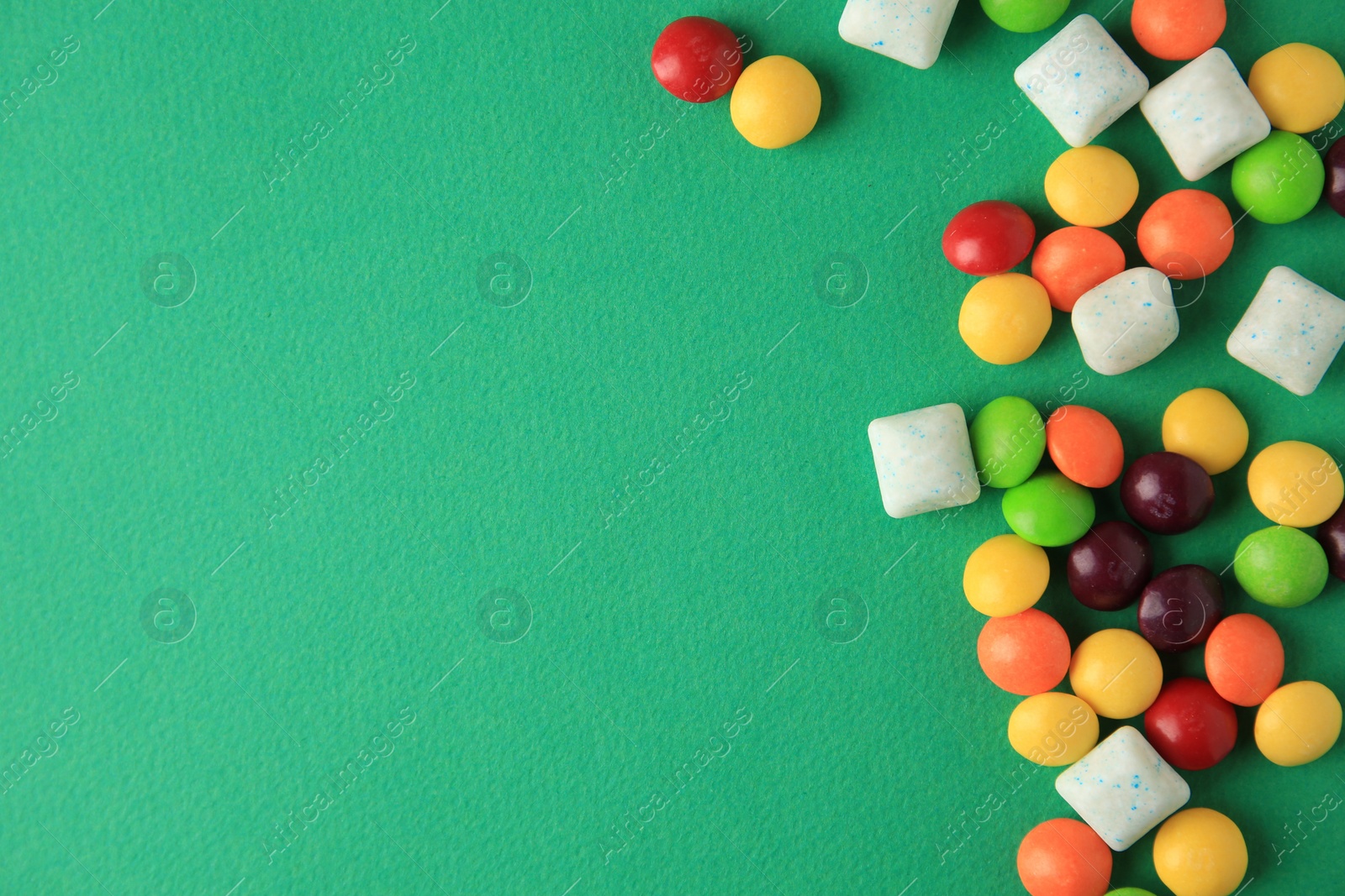 Photo of Different tasty chewing gums on green background, flat lay. Space for text