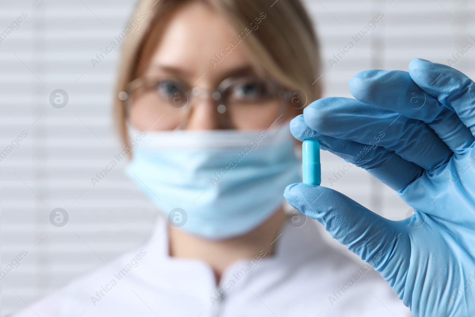 Photo of Doctor holding pill on light background, selective focus. Space for text