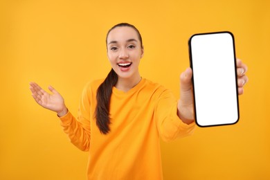 Surprised woman showing smartphone in hand on yellow background