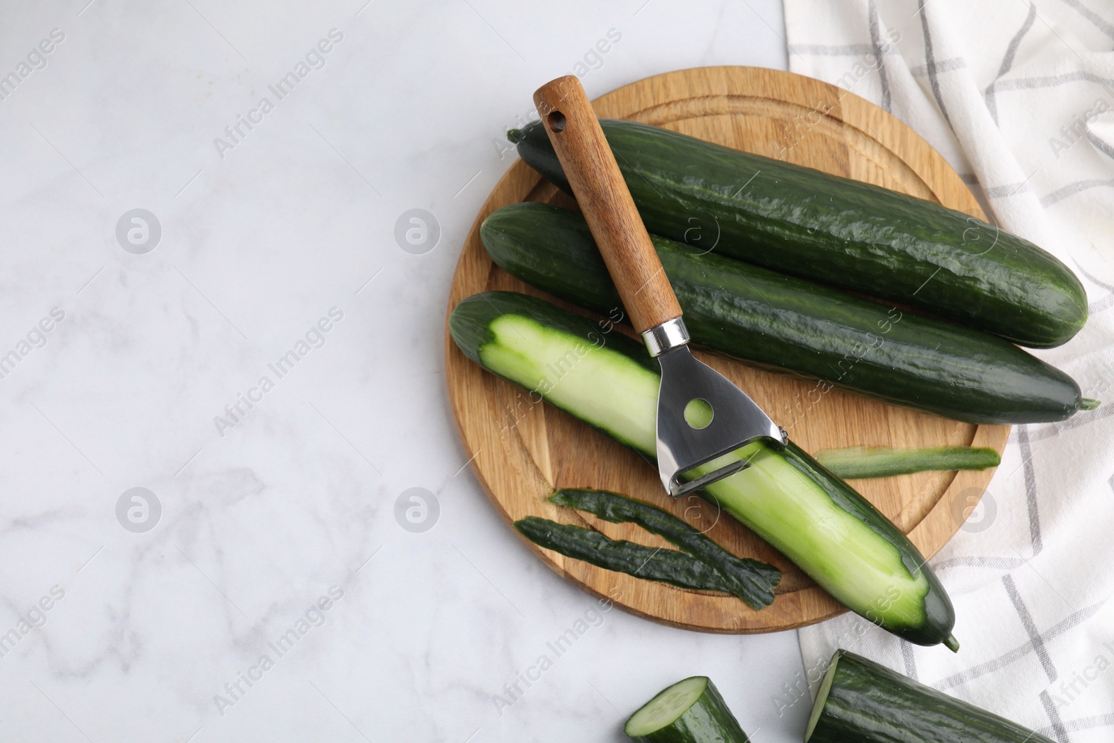 Photo of Fresh cucumbers and peeler on white marble table, top view. Space for text