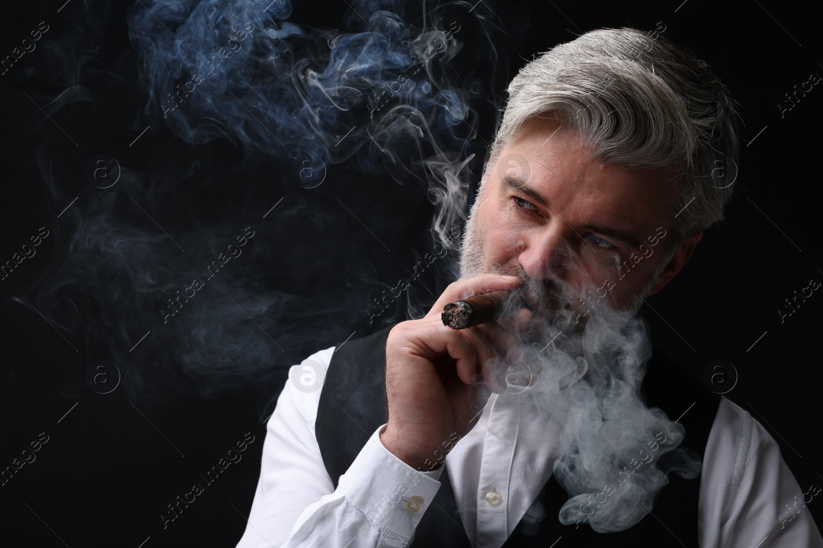 Photo of Bearded man smoking cigar against black background. Space for text