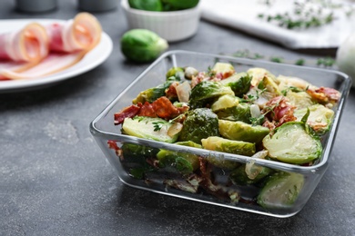 Delicious Brussels sprouts with bacon in glass baking dish on grey table