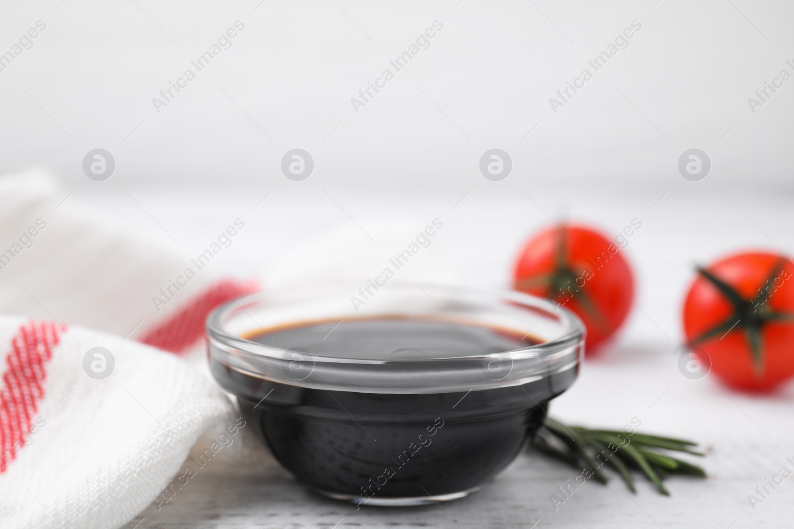 Photo of Bowl with balsamic vinegar, rosemary and tomatoes on white wooden table, closeup