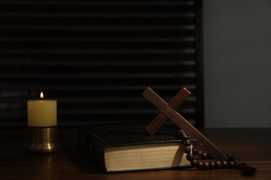 Cross, rosary beads, Bible and church candle on wooden table