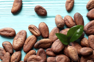 Tasty cocoa beans on blue wooden table, top view