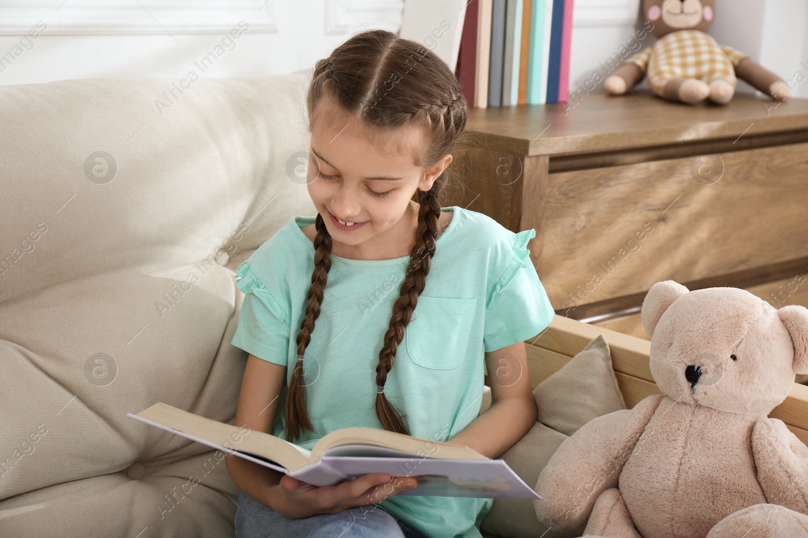 Photo of Cute little girl reading book on sofa at home