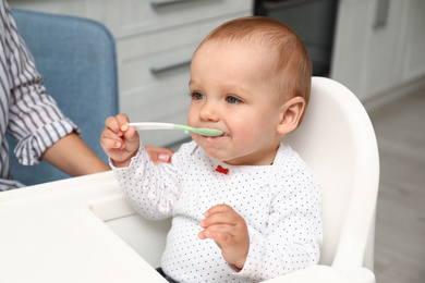 Cute little baby with spoon in highchair at home