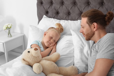 Photo of Father looking at his cute sleeping daughter in bed