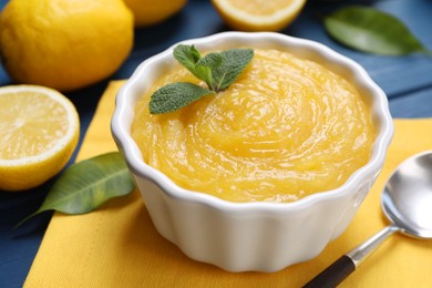 Photo of Delicious lemon curd in bowl, fresh citrus fruits and spoon on table, closeup