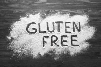 Photo of Words Gluten free written with flour on dark wooden table, top view