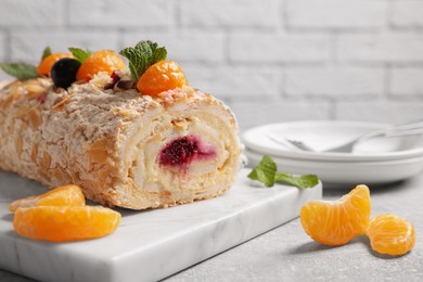 Tasty meringue roll with jam, tangerine slices and mint leaves on grey table, closeup