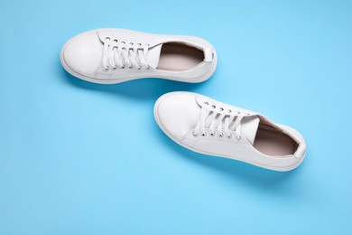 Photo of Pair of stylish white sneakers on light blue background, top view