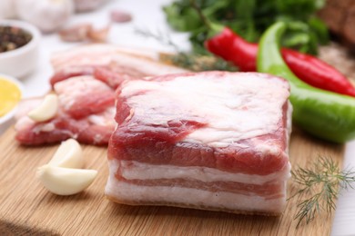 Photo of Pieces of tasty pork fatback with garlic and chilli pepper on wooden table, closeup