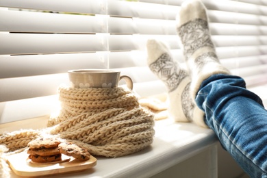 Photo of Woman and cup of hot winter drink near window indoors, closeup