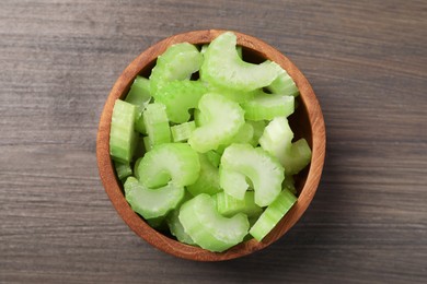 Photo of Bowl with fresh green cut celery on wooden table, top view