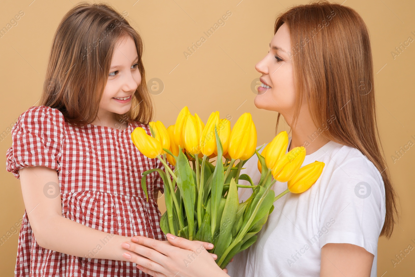 Photo of Mother and her cute daughter with bouquet of yellow tulips on beige background