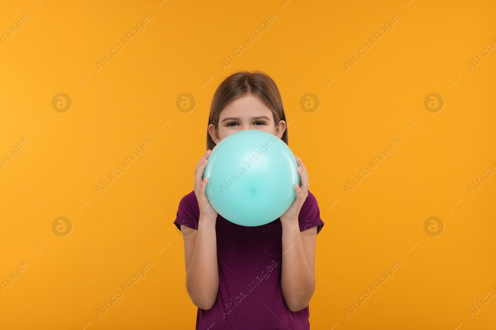 Photo of Girl inflating bright balloon on orange background