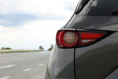Photo of New black modern car on asphalt road, closeup of taillight. Space for text