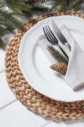 Stylish festive place setting with plate, cutlery and fir branches on white wooden table