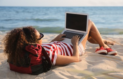 Photo of African American woman working on laptop at beach