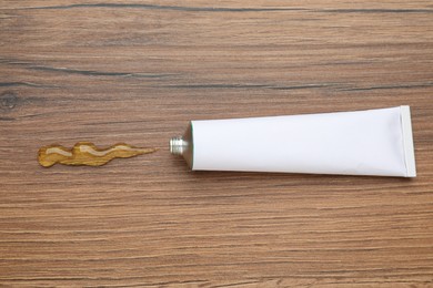 Photo of Open white tube with ointment on wooden table, top view. Space for text