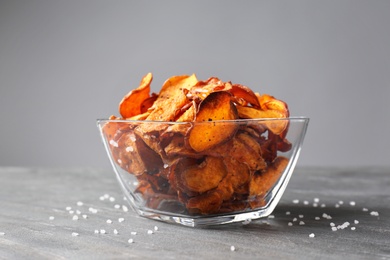Photo of Bowl of sweet potato chips and salt on table against grey background