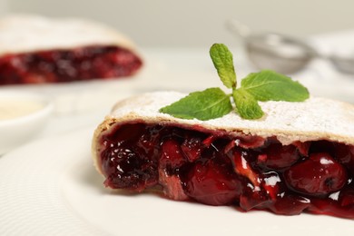 Delicious strudel with cherries, powdered sugar and mint on plate, closeup