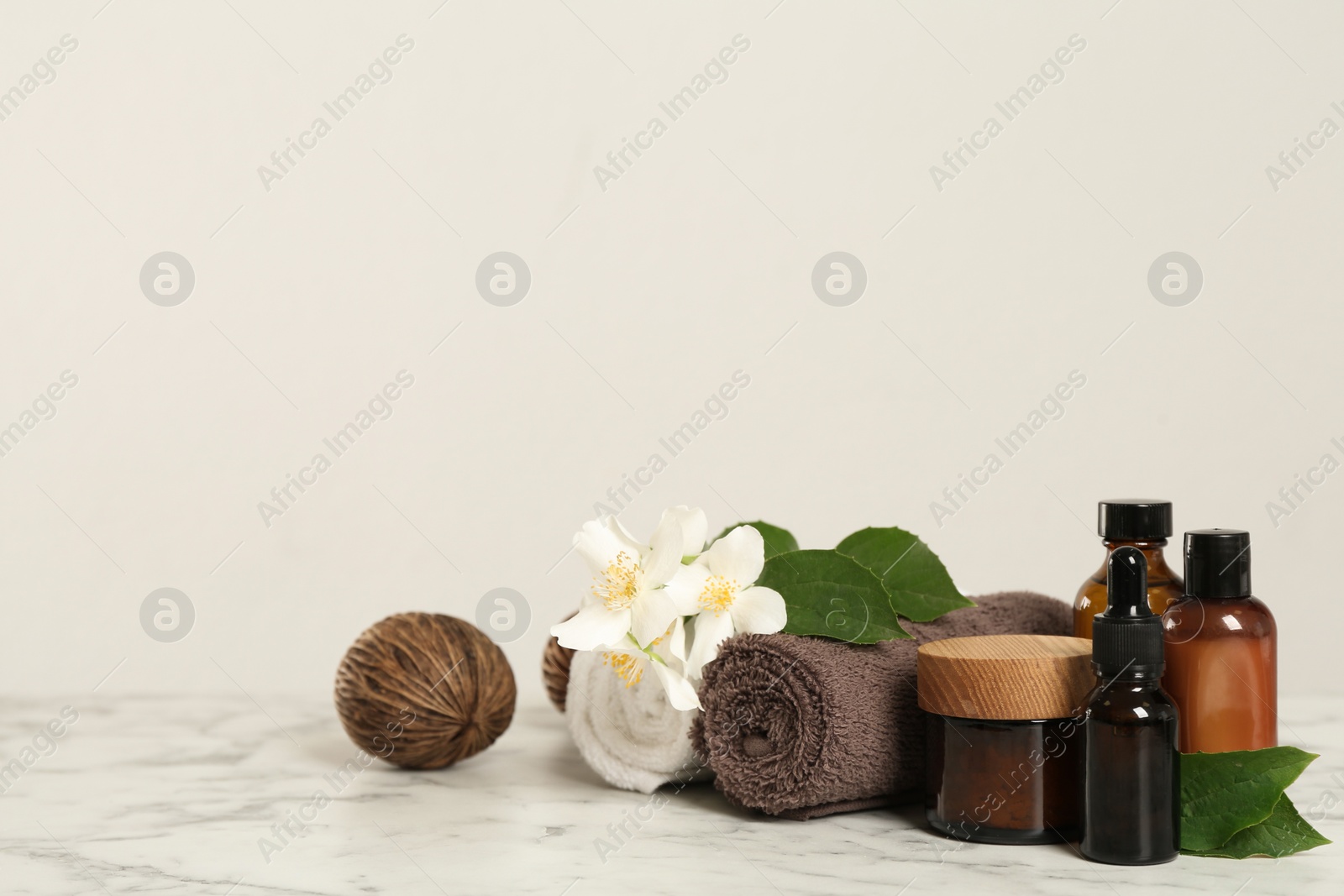 Photo of Beautiful jasmine flowers, skin care products and towels on white marble table, space for text