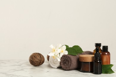 Photo of Beautiful jasmine flowers, skin care products and towels on white marble table, space for text