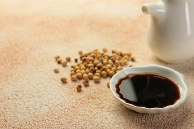 Photo of Soy sauce in bowl and beans on beige textured table. Space for text