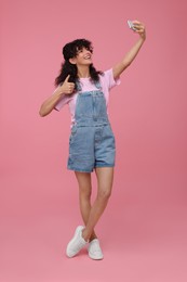 Beautiful young woman taking selfie on pink background