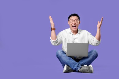 Emotional man with laptop on lilac background, space for text