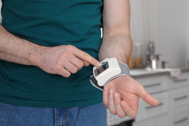 Photo of Young man checking pulse with digital medical device indoors, closeup