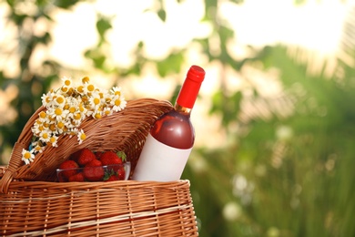 Picnic basket with wine, strawberries and flowers on blurred background, space for text