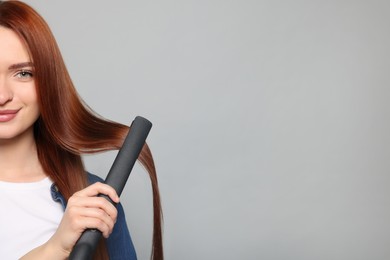 Beautiful woman using hair iron on light gray background, closeup. Space for text