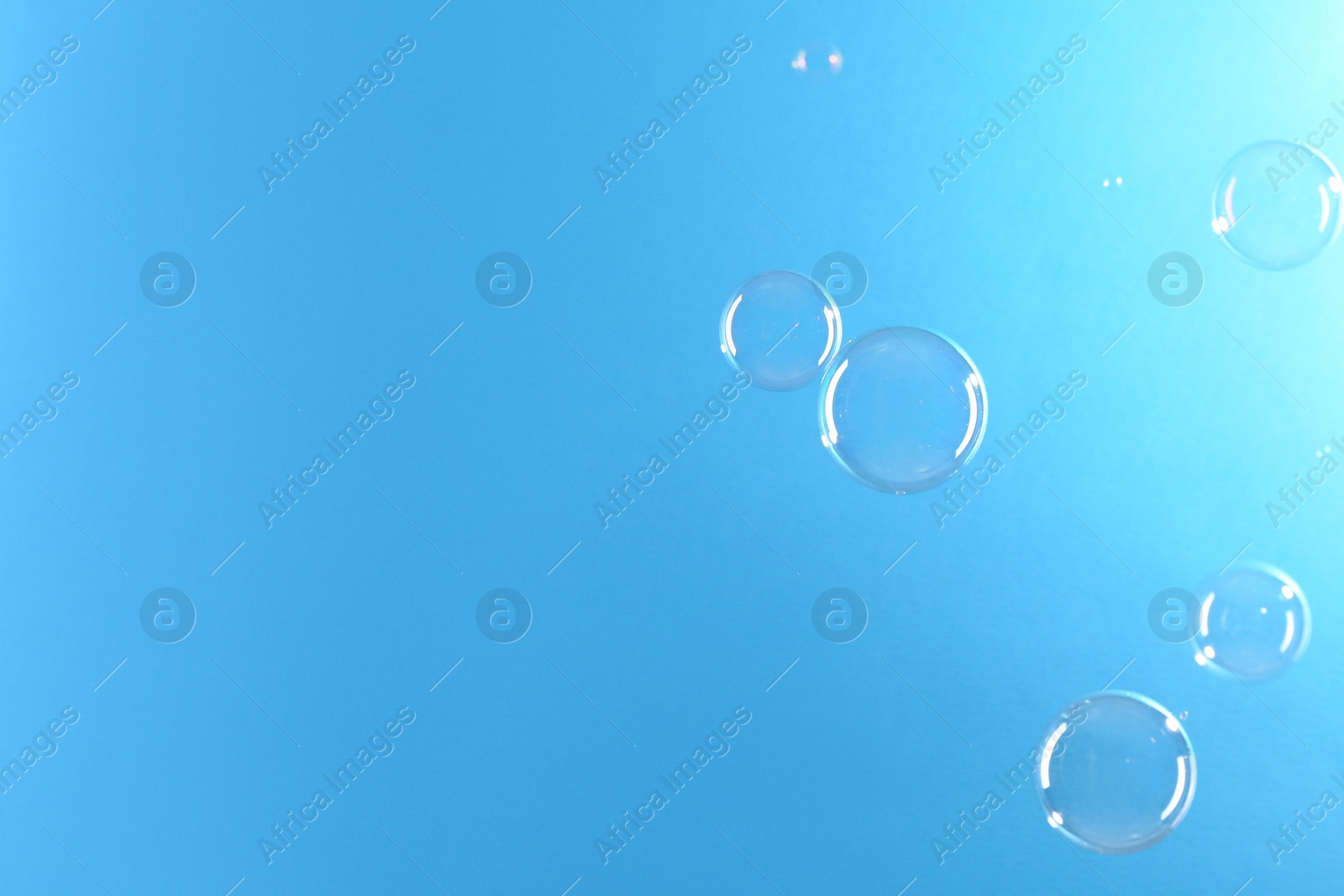 Photo of Beautiful transparent soap bubbles on light blue background, space for text