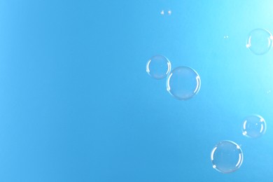 Photo of Beautiful transparent soap bubbles on light blue background, space for text
