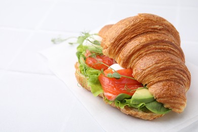Tasty croissant with salmon, avocado, mozzarella and lettuce on white table, closeup. Space for text