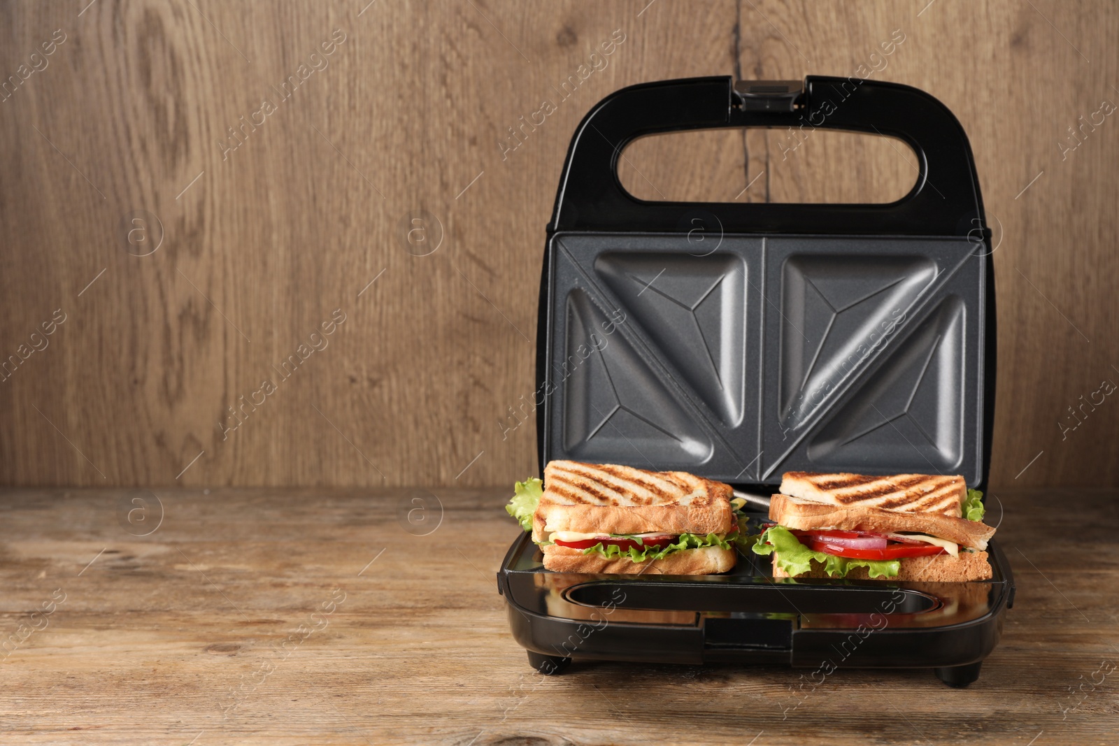 Photo of Modern grill maker with sandwiches on wooden table, space for text