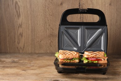 Modern grill maker with sandwiches on wooden table, space for text