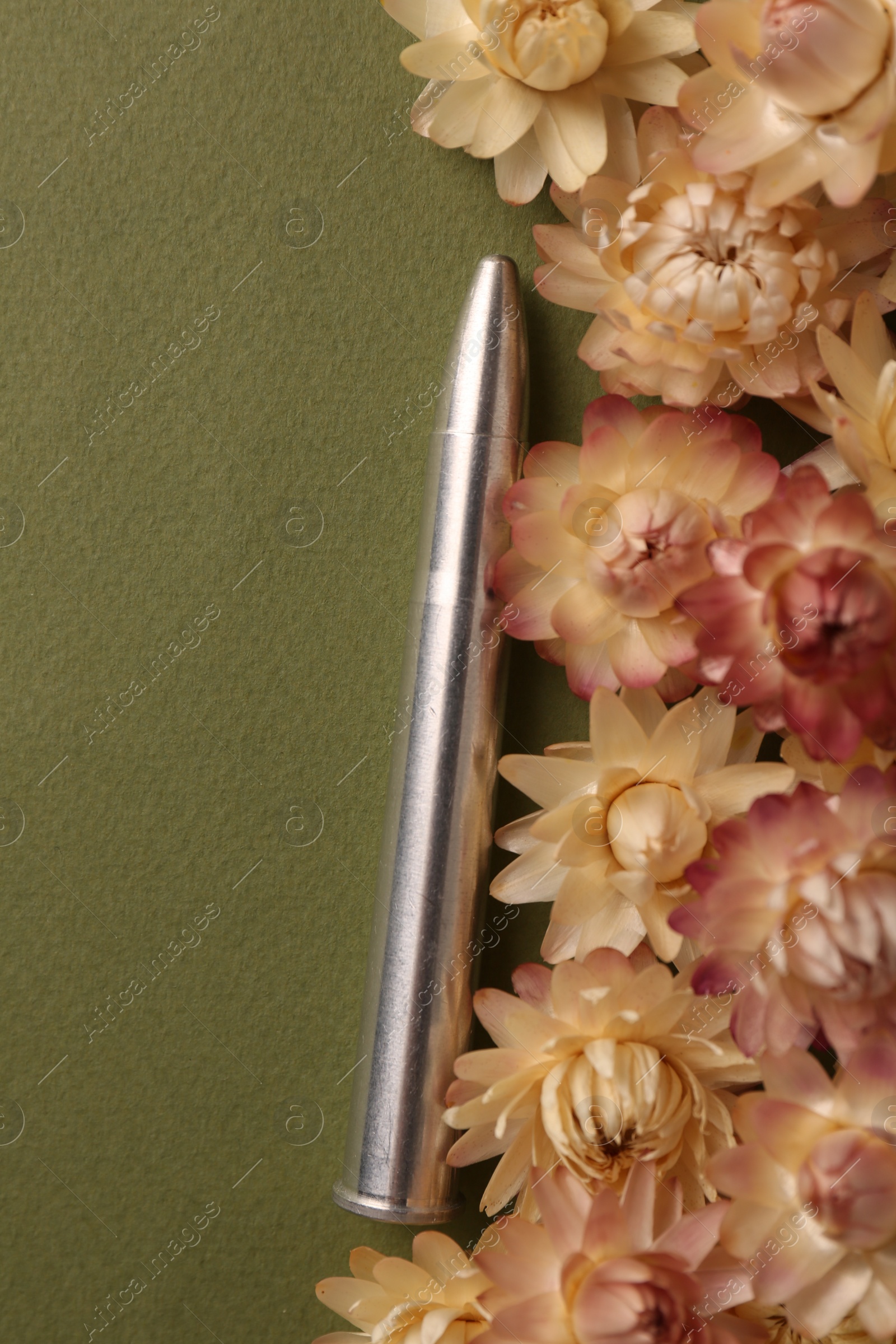 Photo of One bullet and beautiful flowers on green background, flat lay. Space for text