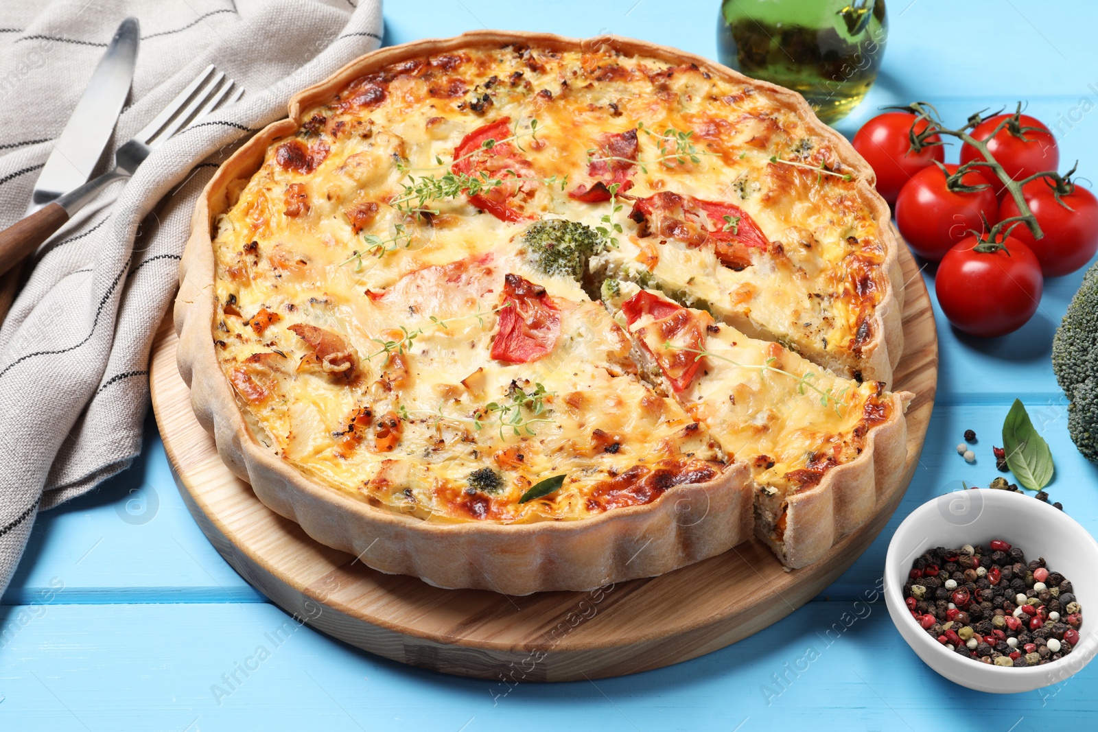 Photo of Tasty quiche with tomatoes, microgreens and cheese served on light blue wooden table, closeup