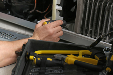 Image of Electrician with screwdriver fixing refrigerator indoors, closeup 