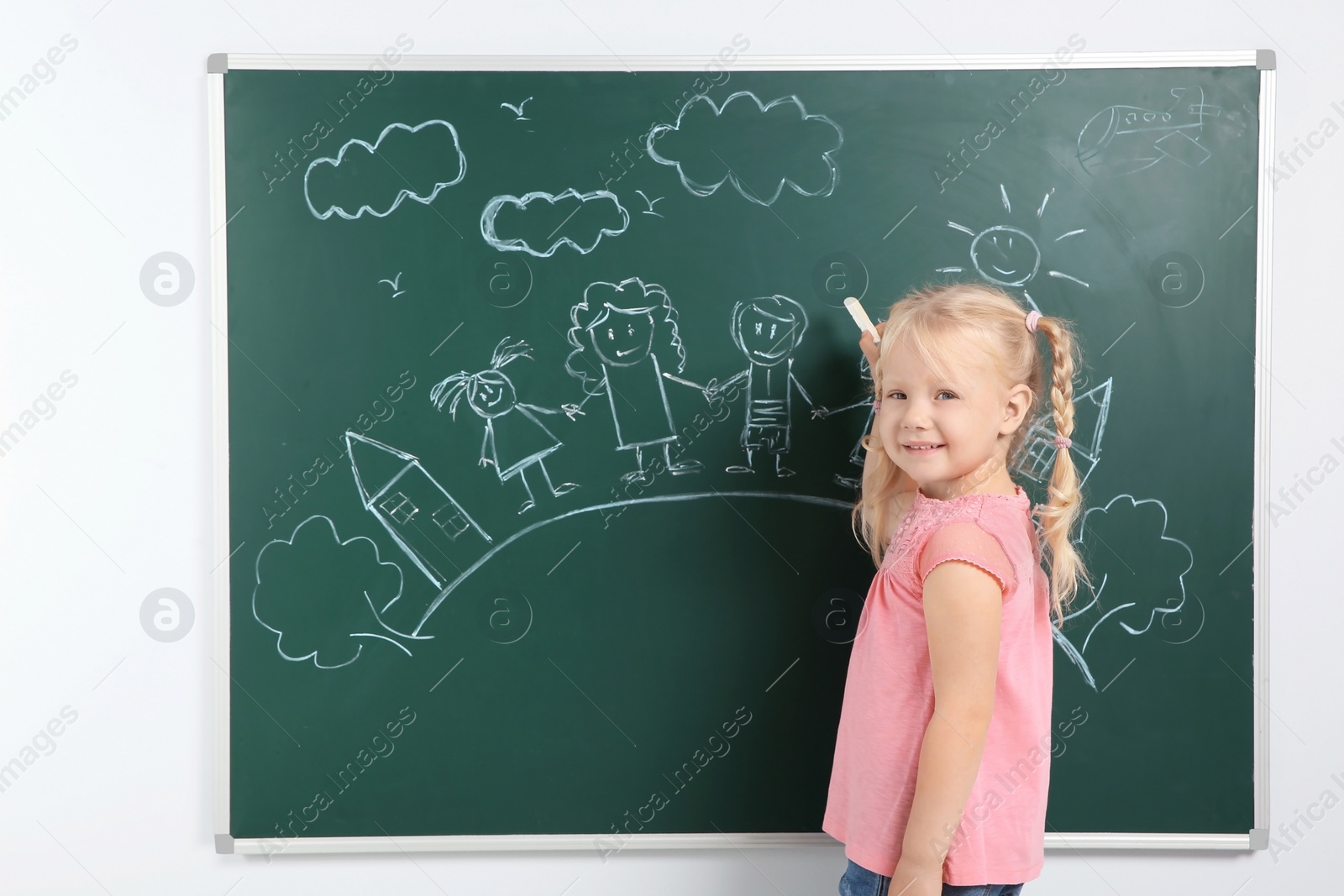 Photo of Little child drawing family with white chalk on blackboard