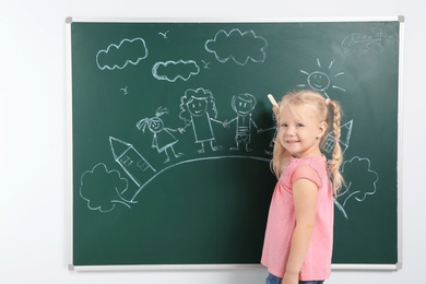 Photo of Little child drawing family with white chalk on blackboard