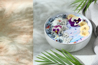 Delicious smoothie bowl with fresh fruits, blueberries and flowers on color textured table. Space for text