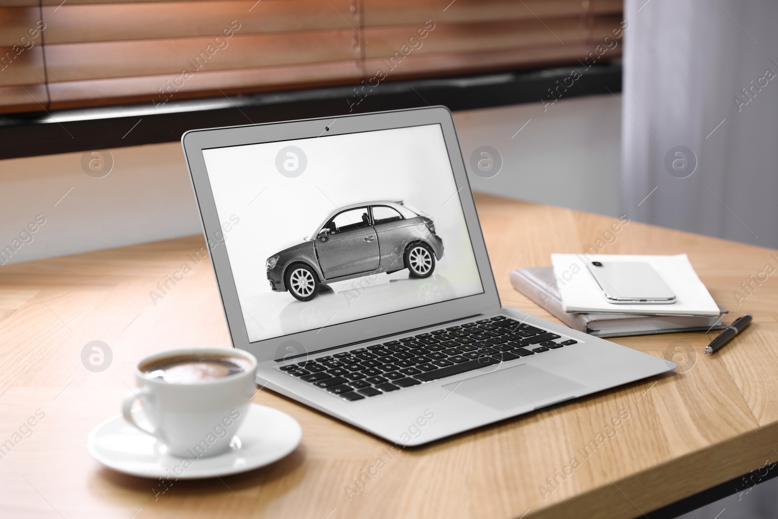 Photo of Laptop screen with automobile on wooden table. Car buying`