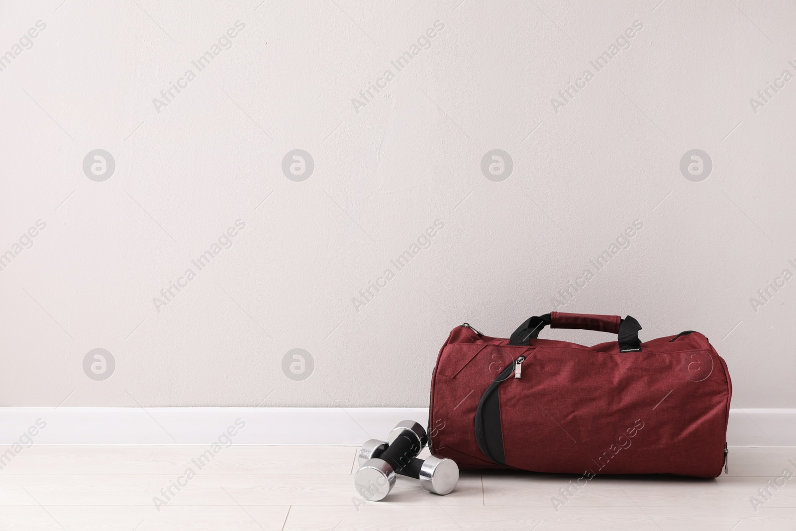 Photo of Red sports bag and dumbbells on floor near light wall, space for text