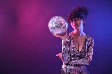 Photo of Beautiful young woman with disco ball posing on color background in neon lights. Space for text